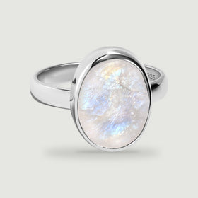 An oval moonstone with blue and peach reflections sits in a polished sterling silver ring.