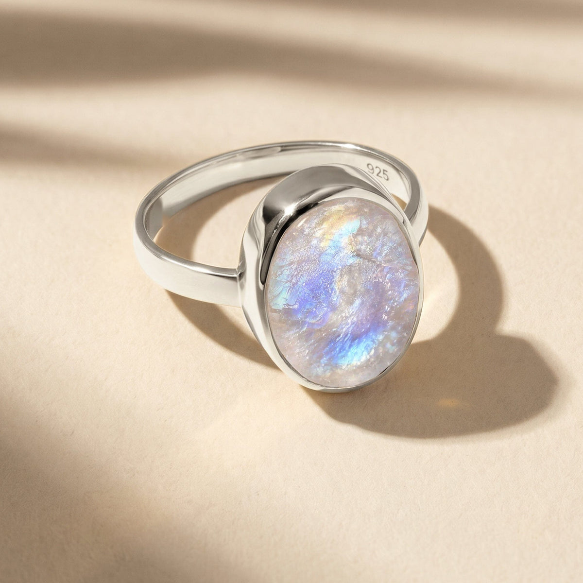 A silver moonstone ring rests on a pale textured tabletop with a shadow falling to the right.
