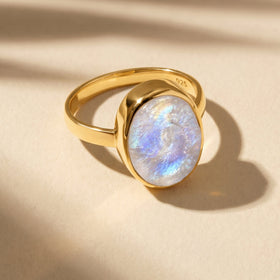 A yellow gold vermeil moonstone ring lies on a cream surface with warm light across its band.