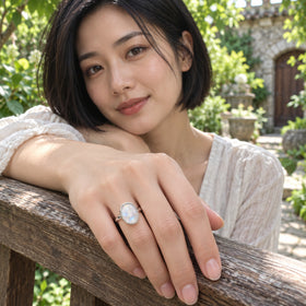 A silver moonstone ring is visible on a relaxed hand resting over a wooden garden railing.