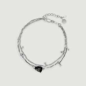 A complete silver bracelet with a black irregular stone, curved links, a fine chain, and an extender rests on light gray.