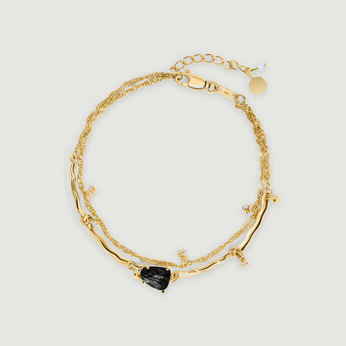A yellow gold bracelet forms an oval with a dark textured stone at the front and a clasp at the top.