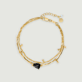 A yellow gold bracelet forms an oval with a dark textured stone at the front and a clasp at the top.