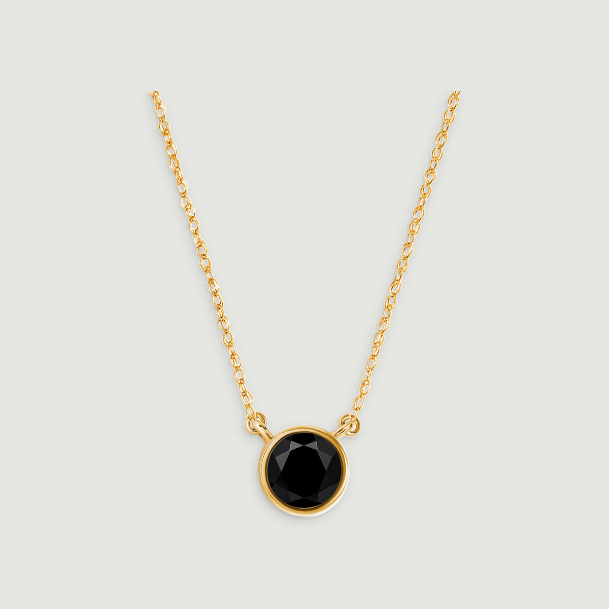 A round faceted black onyx pendant hangs between yellow gold chain links on a pale gray background.