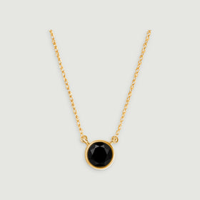 A round faceted black onyx pendant hangs between yellow gold chain links on a pale gray background.