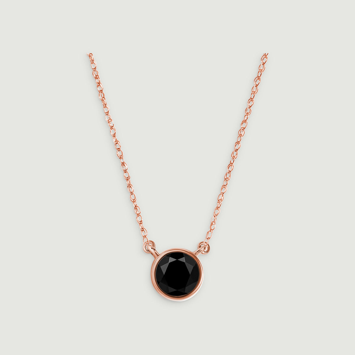 A rose gold necklace with a single round black pendant is centered against a light gray surface.