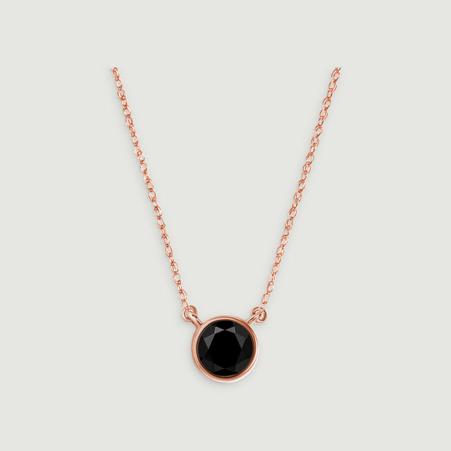 A rose gold necklace with a single round black pendant is centered against a light gray surface.