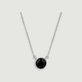A circular black onyx pendant sits between two lengths of white gold chain on a gray background.
