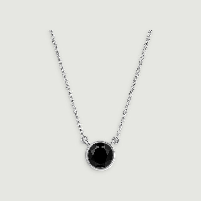 A circular black onyx pendant sits between two lengths of white gold chain on a gray background.