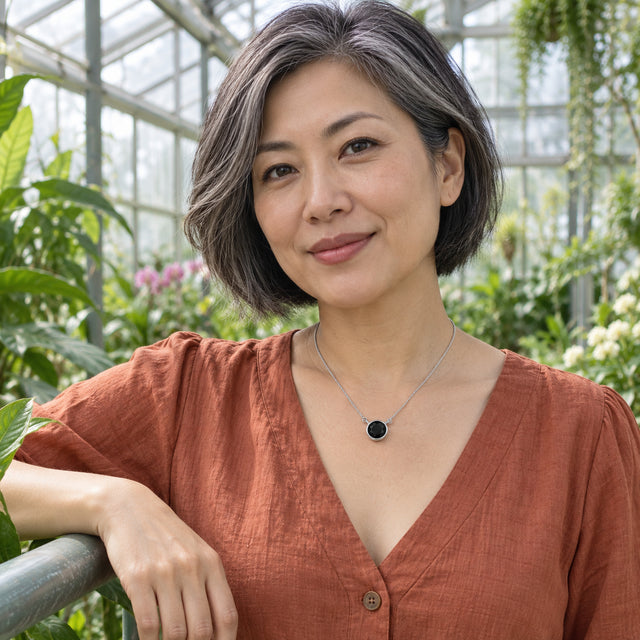 A woman in a terracotta blouse wears the white gold black onyx necklace among greenhouse plants.