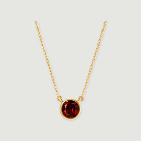 A round red garnet in a yellow gold bezel hangs between two lengths of fine chain on a light gray background.