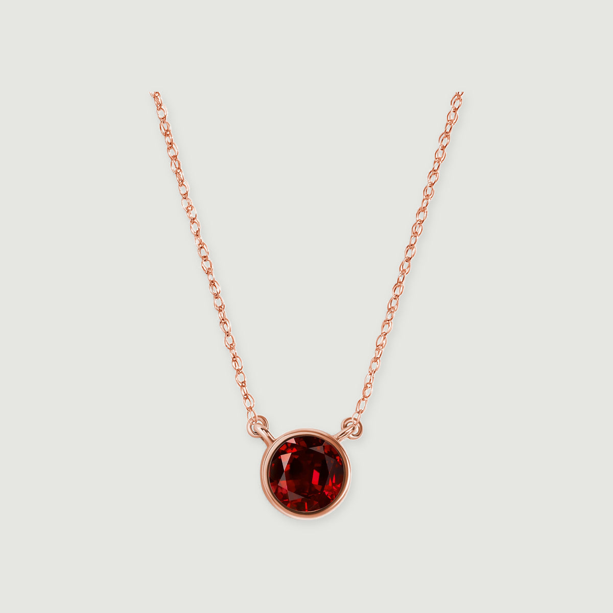 A polished rose gold bezel surrounds a faceted red garnet, with the chain rising on both sides.