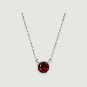 A white gold necklace displays a deep red round garnet against a softly shaded light gray surface.