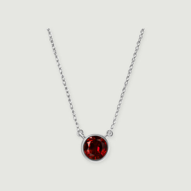 A white gold necklace displays a deep red round garnet against a softly shaded light gray surface.