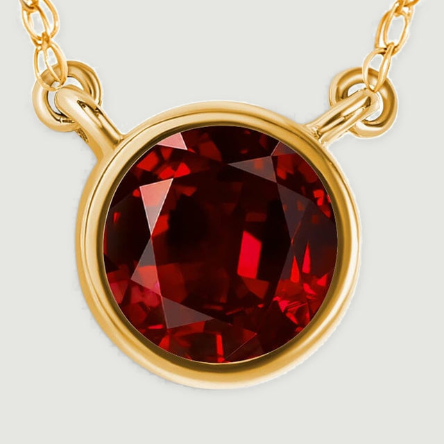 A close view shows the red garnet facets, smooth yellow gold rim, and two small chain connectors.