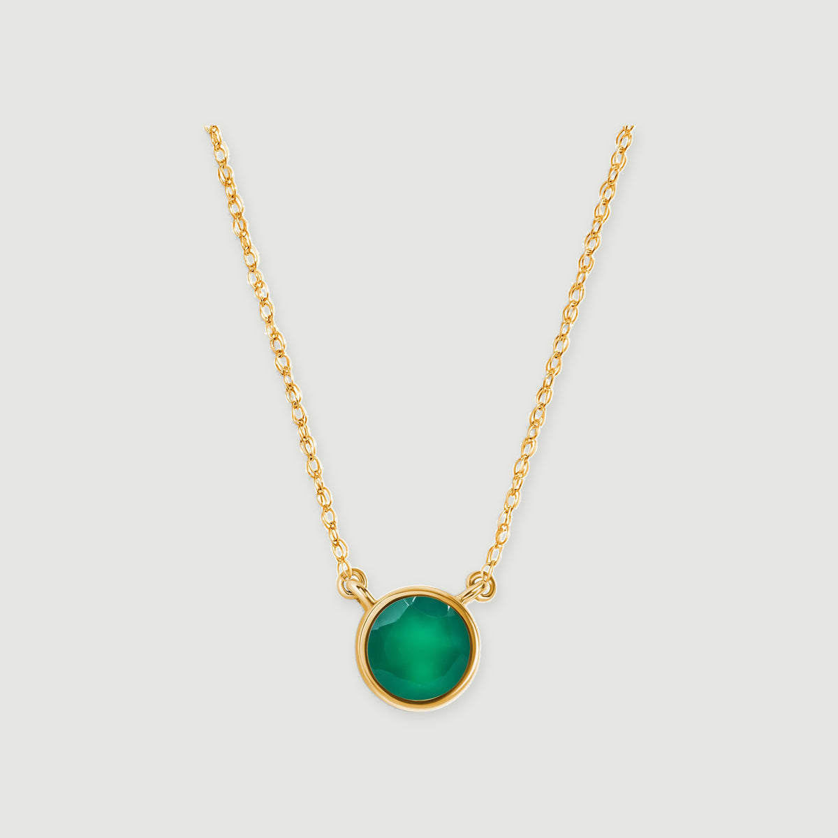 A round green onyx pendant in yellow gold hangs between two fine chain sections on a light gray background.