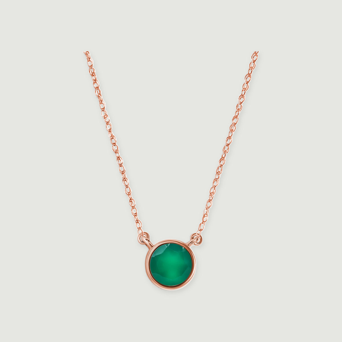 A rose gold necklace with a circular green onyx bezel is centered against a pale gray surface.