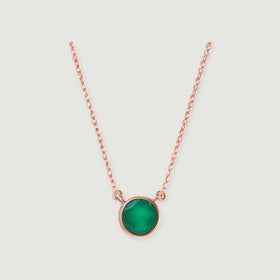 A rose gold necklace with a circular green onyx bezel is centered against a pale gray surface.