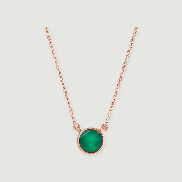 A rose gold necklace with a circular green onyx bezel is centered against a pale gray surface.