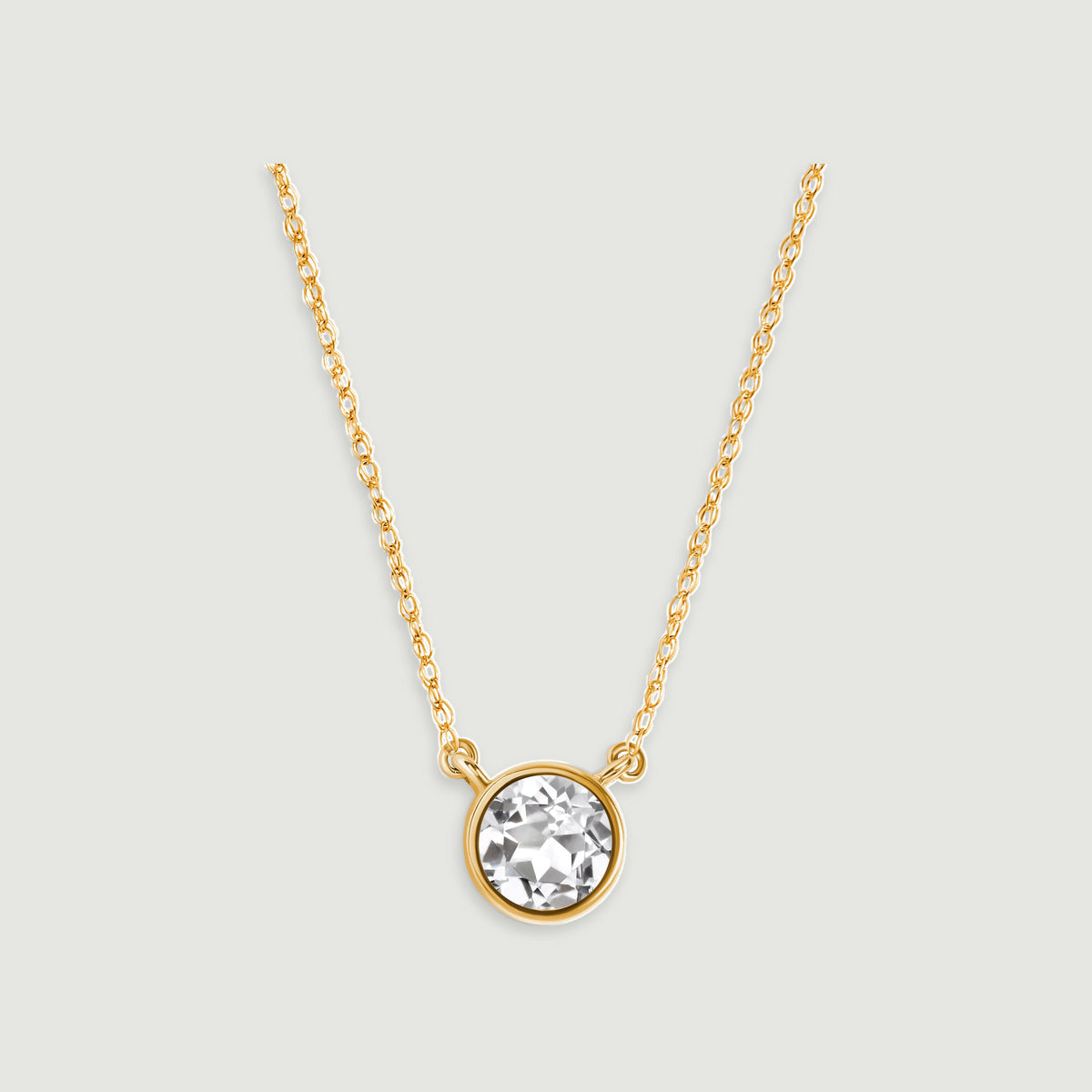 A round clear white topaz in a yellow gold bezel hangs from an oval-link chain on a light gray background.