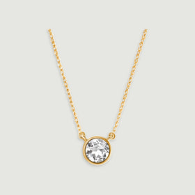 A round clear white topaz in a yellow gold bezel hangs from an oval-link chain on a light gray background.