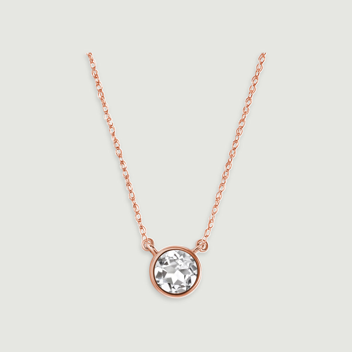 A rose gold chain meets the two side loops of a circular white topaz pendant against pale gray.