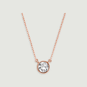 A rose gold chain meets the two side loops of a circular white topaz pendant against pale gray.