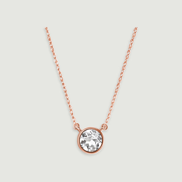 A rose gold chain meets the two side loops of a circular white topaz pendant against pale gray.