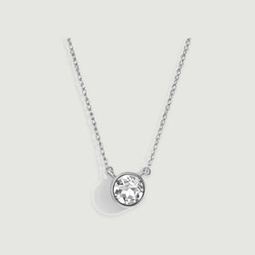 A polished white gold bezel surrounds a faceted clear stone beneath a fine chain on gray.