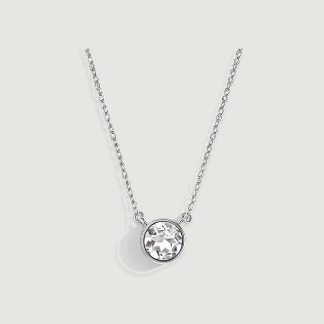 A polished white gold bezel surrounds a faceted clear stone beneath a fine chain on gray.