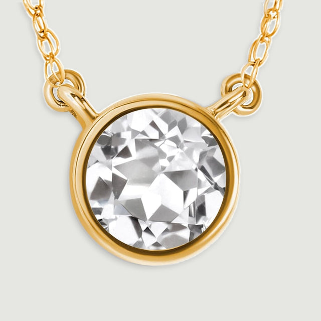 A close view shows the white topaz facets, smooth yellow gold rim, and paired chain connectors.