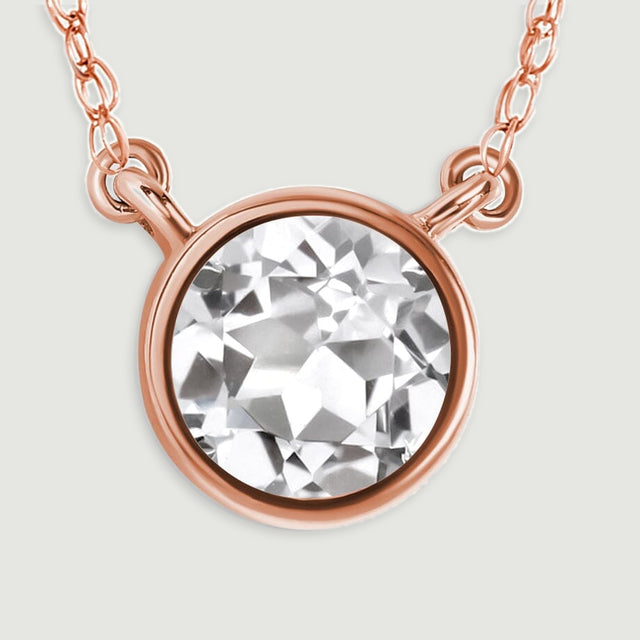 The clear circular gemstone and warm rose gold bezel fill a close view with chain links above.