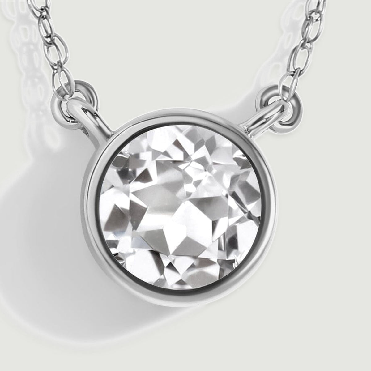 A close-up reveals angular white topaz facets inside a white gold rim with two side attachment loops.