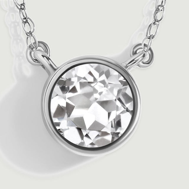 A close-up reveals angular white topaz facets inside a white gold rim with two side attachment loops.