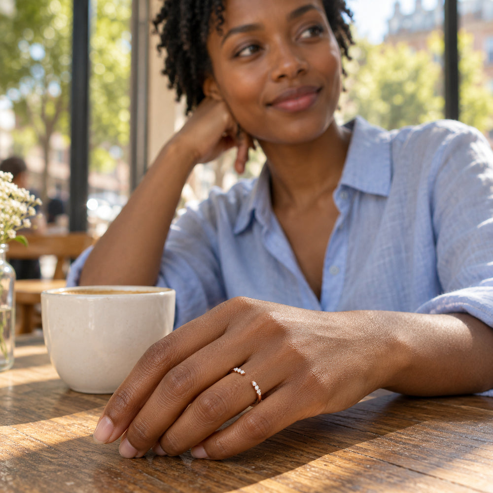 A woman wears the rose gold open diamond ring while resting her hand on a wooden cafe table beside a ceramic cup.