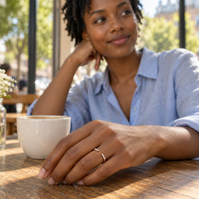 A woman wears the rose gold open diamond ring while resting her hand on a wooden cafe table beside a ceramic cup.