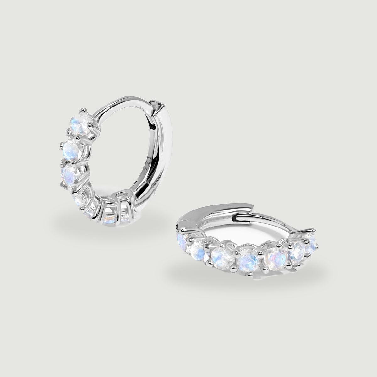 Two polished silver moonstone hoops rest at different angles on a light gray surface.