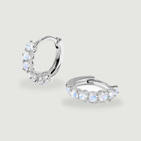 Two polished silver moonstone hoops rest at different angles on a light gray surface.