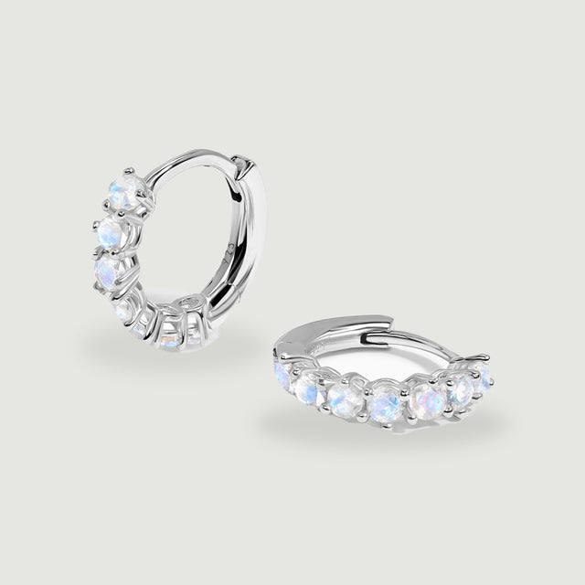 Two polished silver moonstone hoops rest at different angles on a light gray surface.
