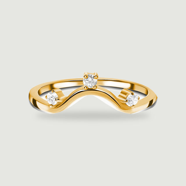 Three clear round stones follow the curved front of a yellow gold ring on light grey.