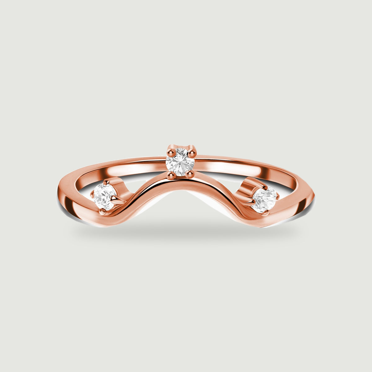 A rose gold wave ring with three bright round stones is centred above a soft shadow.