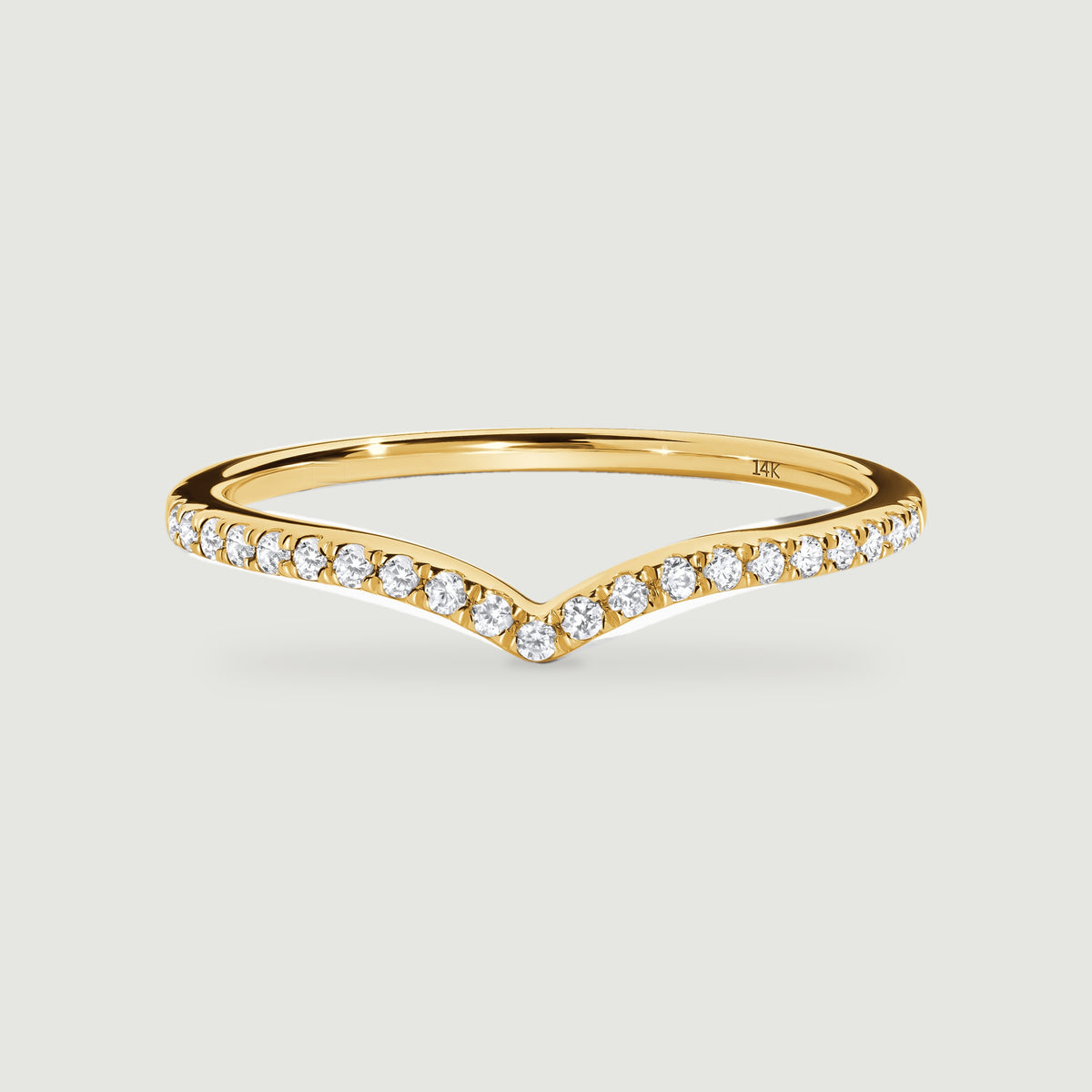 A yellow gold ring has a shallow V-shaped front lined with round diamonds on a light grey surface.