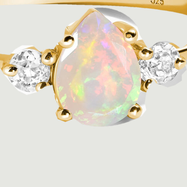 A close view shows the opal flashing pink and green between yellow gold prongs and clear side stones.