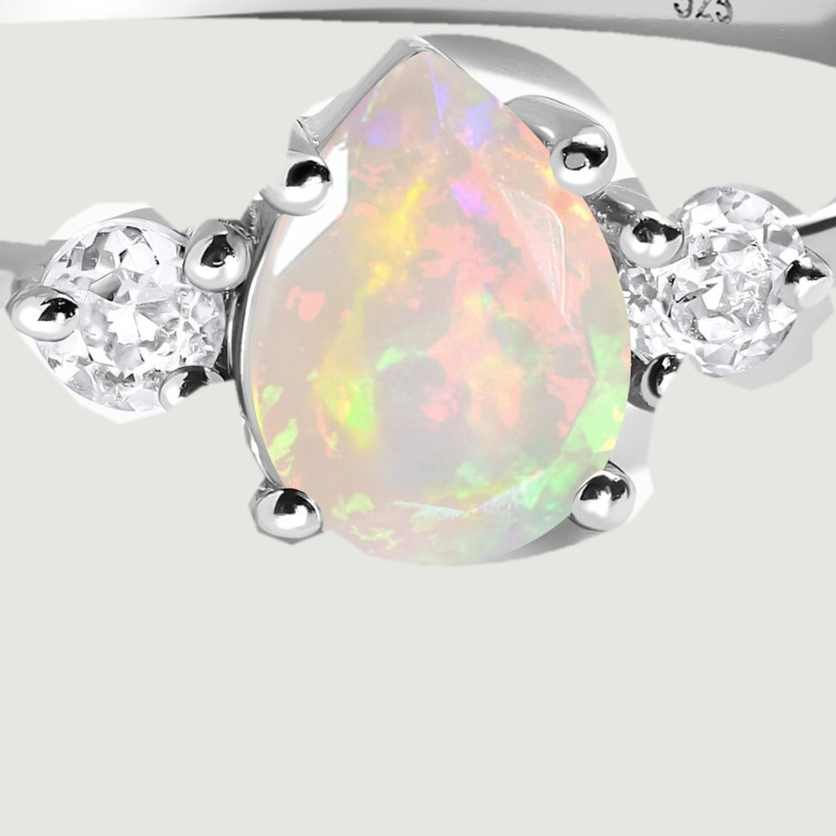 Silver prongs hold the pear-shaped opal beside two round faceted stones in this close view.