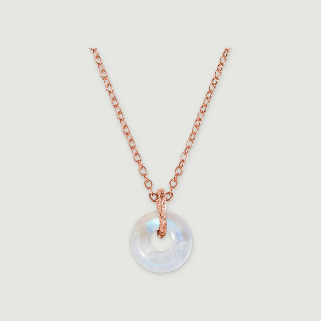 A circular moonstone pendant hangs from a rose gold chain against a light gray background.