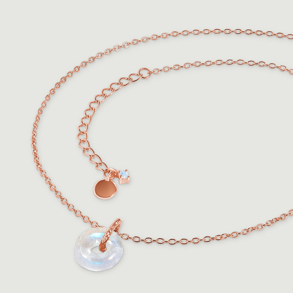 The rose gold necklace lies in a curved arrangement with its extender and small end stone visible.