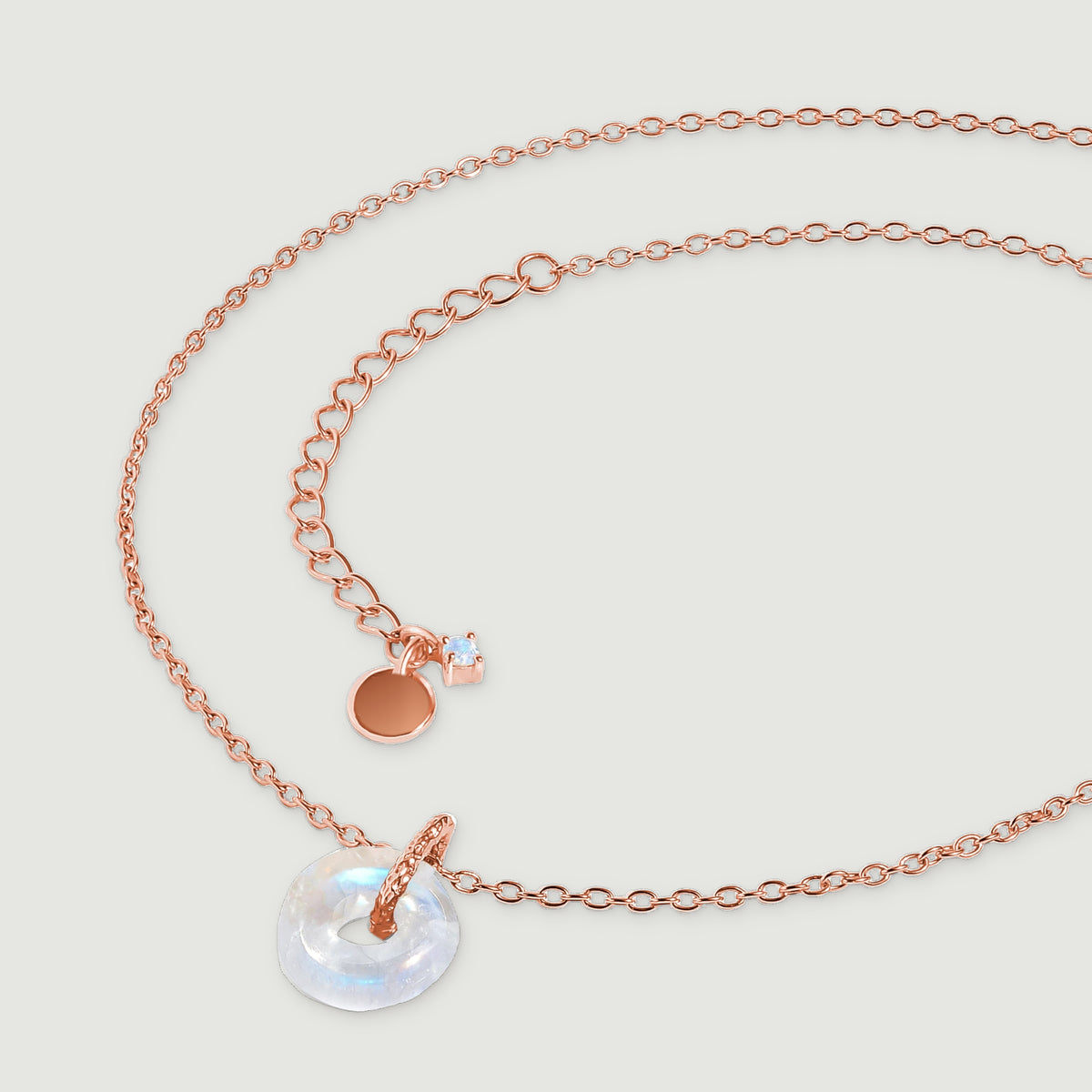 The rose gold necklace lies in a curved arrangement with its extender and small end stone visible.