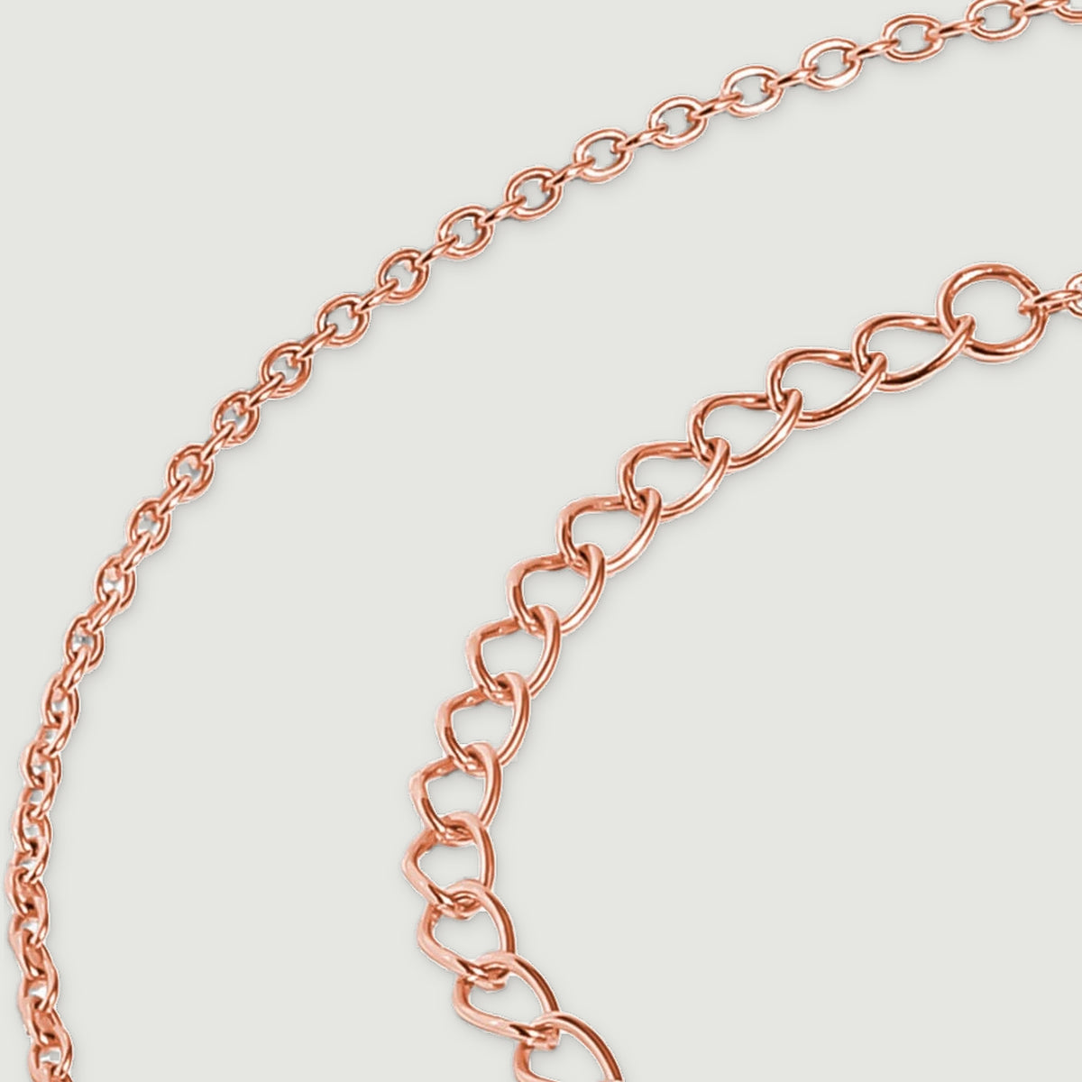 Oval rose gold extender links curve beside the finer links of the necklace chain.