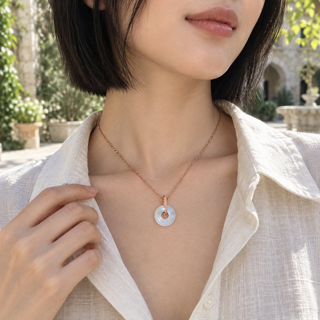 A woman in a cream linen shirt wears the rose gold moonstone necklace in a sunlit courtyard.