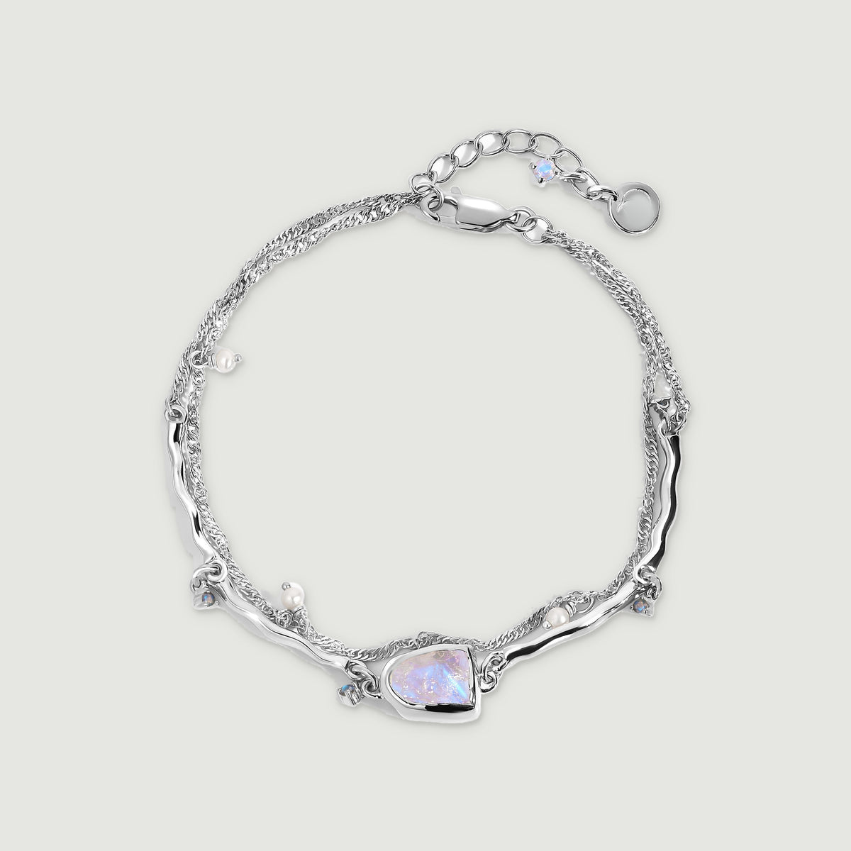 A sterling silver bracelet forms an oval with a raw moonstone, small pearls, blue charms, and an extender chain.